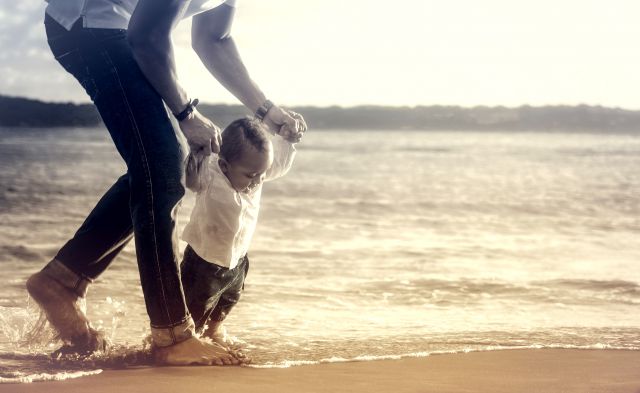 s_Baby_Taking_First_Steps_with_Fathers_Help_on_the_Beach